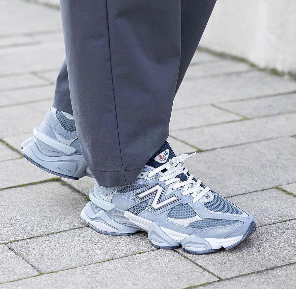 WhatsApp_Image_2024-10-26_at_16.18.03 | AE JERSEY Pair of gray New Balance sneakers worn with gray pants on a paved sidewalk, ready for a walk.
