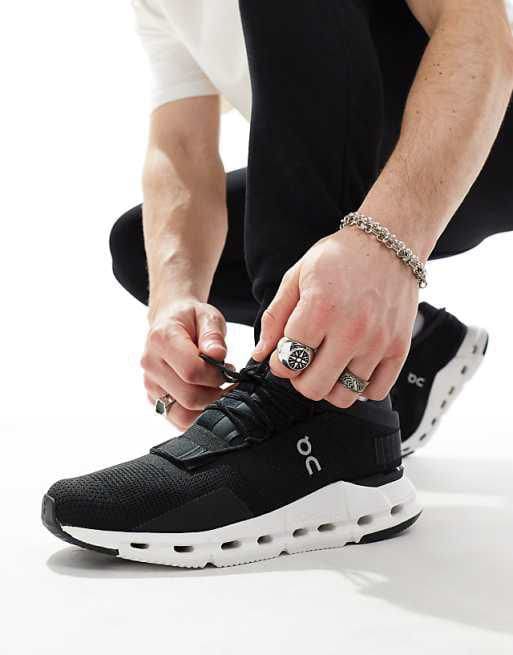 WhatsApp_Image_2024-11-07_at_12.03.04 | AE JERSEY Person tying the laces of a black On running shoe with a white sole on a light background.