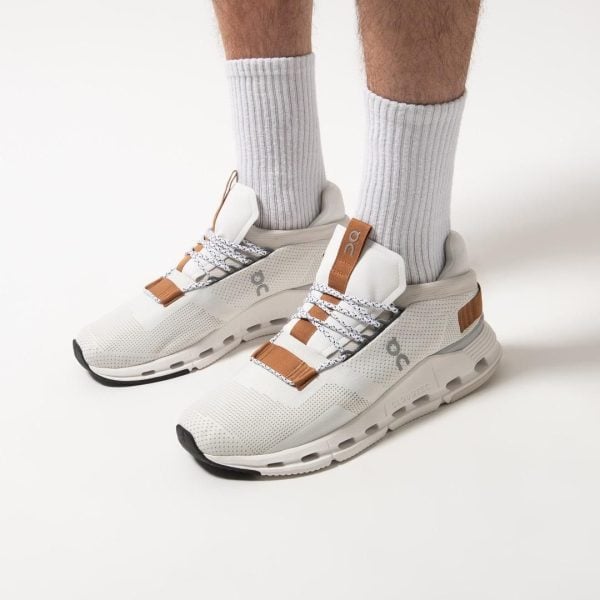 White athletic sneakers with tan-brown accents worn with light gray ribbed socks on a pale backdrop (showing a sporty lifestyle product).