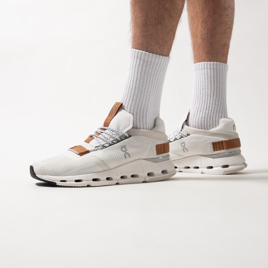 WhatsApp_Image_2024-11-07_at_14.08.44 | AE JERSEY Pair of cream-colored running sneakers with brown leather straps and gray laces, worn with light gray ribbed socks on a white backdrop, showing a chunky midsole.
