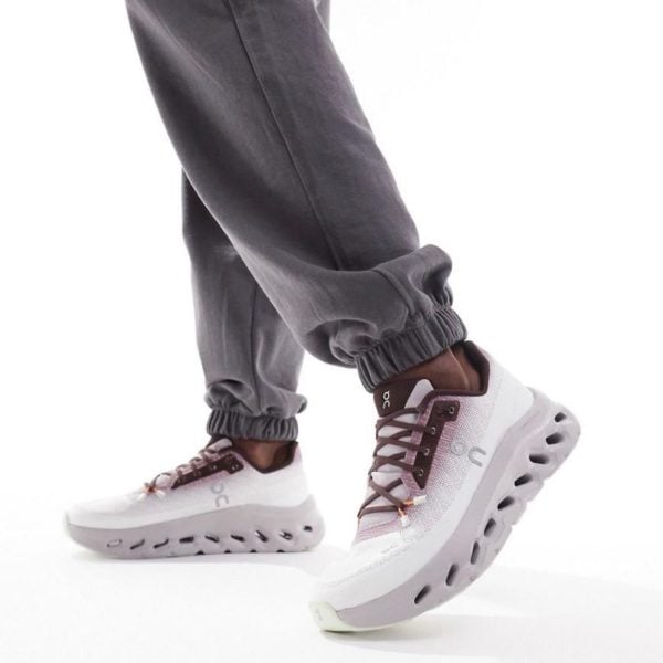 White and pastel pink running shoes with a chunky perforated sole, worn with gray joggers .