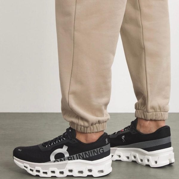 Beige joggers with black On running sneakers featuring a chunky white sole and visible cutouts at the bottom.