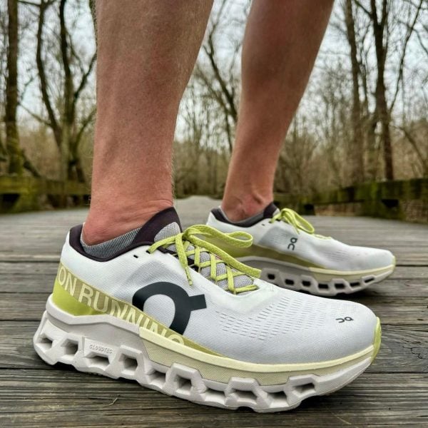 Close-up of white On running shoes with lime green laces on a wooden boardwalk.