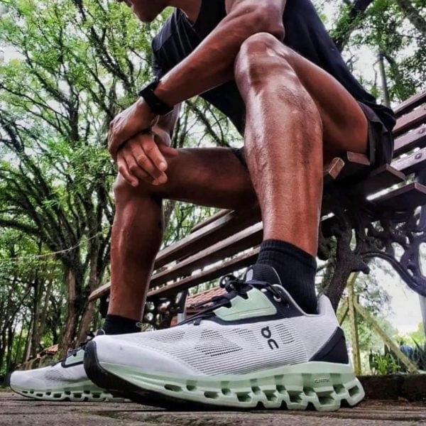Close-up of a person tying the laces of white mint trail running shoes while sitting on a park bench outdoors.