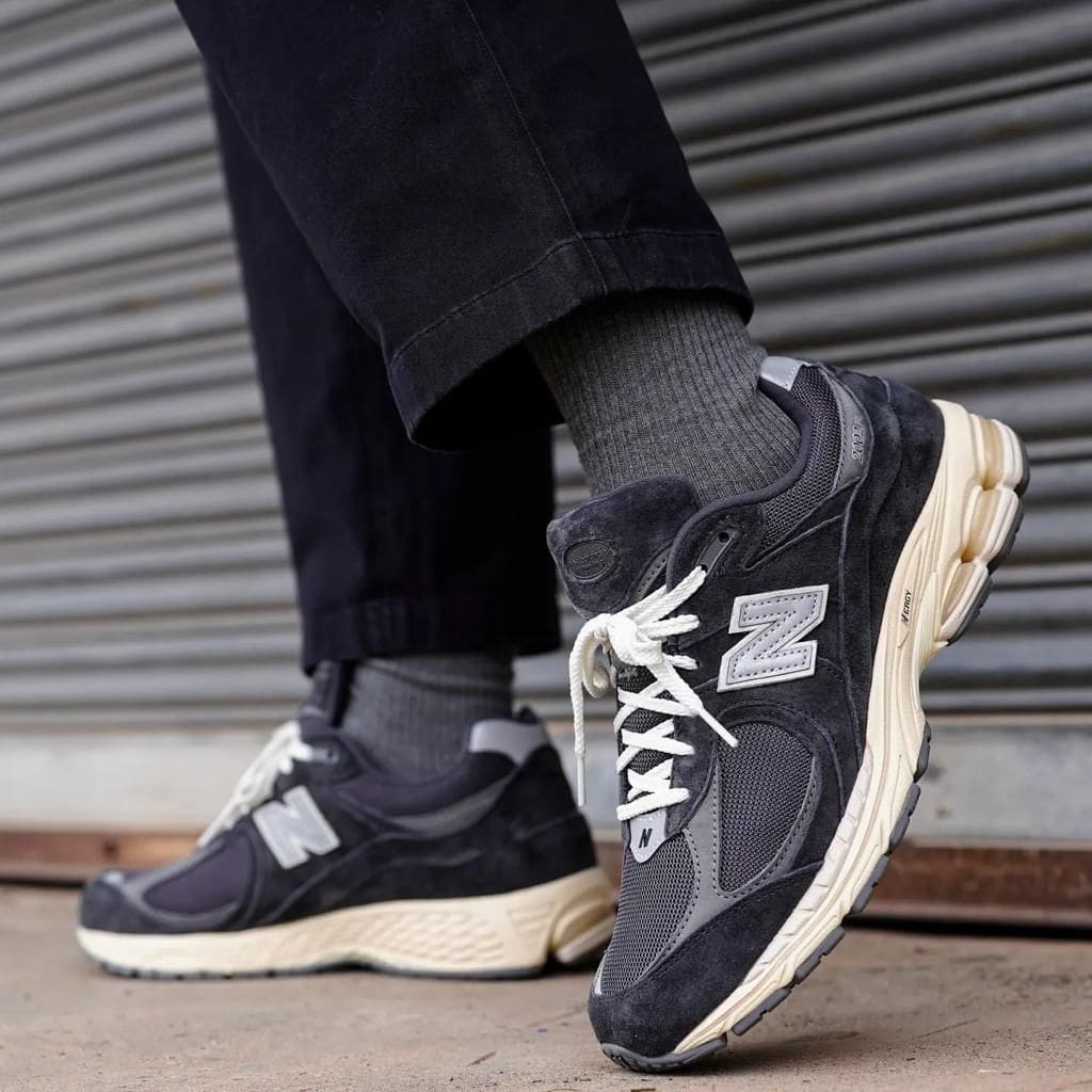 WhatsApp_Image_2024-12-17_at_11.13.01 | AE JERSEY Close-up of grey and black New Balance sneakers with white laces, worn with dark jeans, on a city sidewalk.