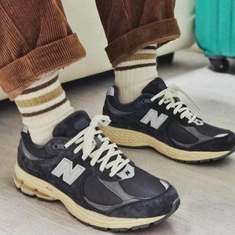 WhatsApp_Image_2024-12-17_at_11.13.07 | AE JERSEY Person wearing black New Balance sneakers with cream soles, cream laces, and striped socks, standing on a light floor with rolled brown pants.