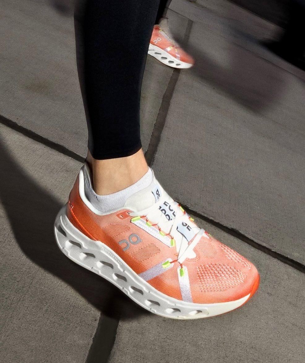 WhatsApp_Image_2025-01-16_at_10.25.31 | AE JERSEY Person wearing coral running shoe with white sole on a sidewalk; black leggings and white sock visible inside the shoe.