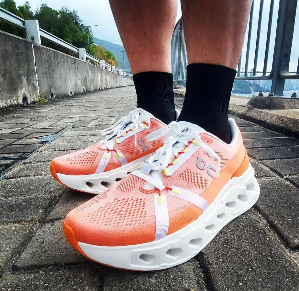 WhatsApp_Image_2025-01-16_at_10.25.39 | AE JERSEY Peach-colored running shoes with white laces and a hollow white sole on a brick walkway beside a railing by the water.