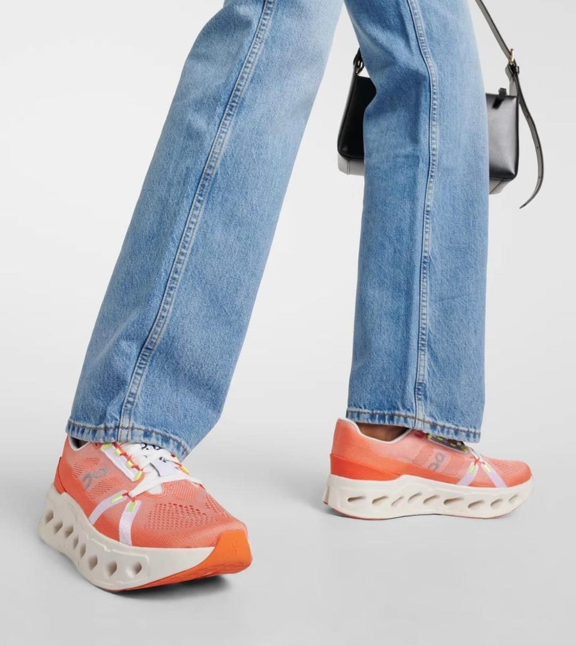WhatsApp_Image_2025-01-16_at_10.25.46 | AE JERSEY Person walking in bright orange sneakers with a white sculpted sole, paired with wide-leg jeans and a small black crossbody bag behind.