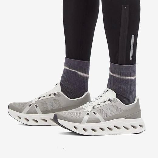 WhatsApp_Image_2025-01-16_at_15.08.35 | AE JERSEY Gray athletic sneakers with a perforated, sculpted white sole, worn with purple tie-dye socks and black leggings with a zipper pocket.