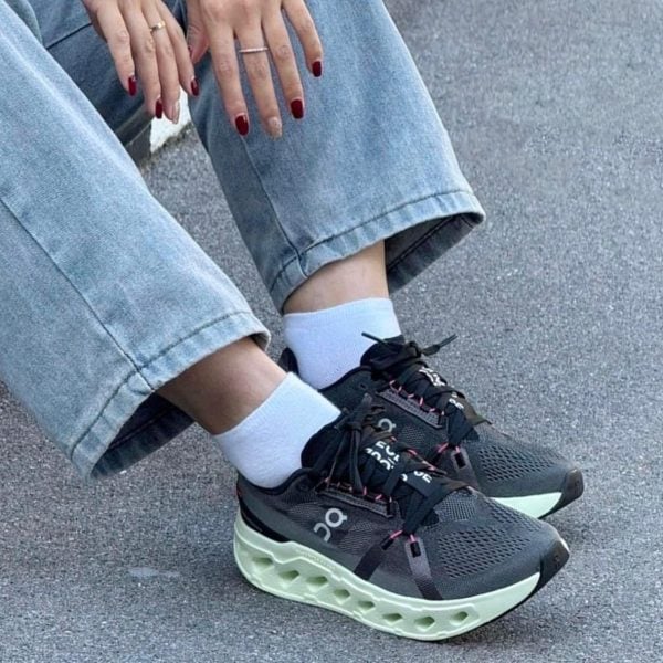 Close-up of feet in dark athletic sneakers with a mint-green chunky sole, white socks, and cuffed light-wash jeans.
