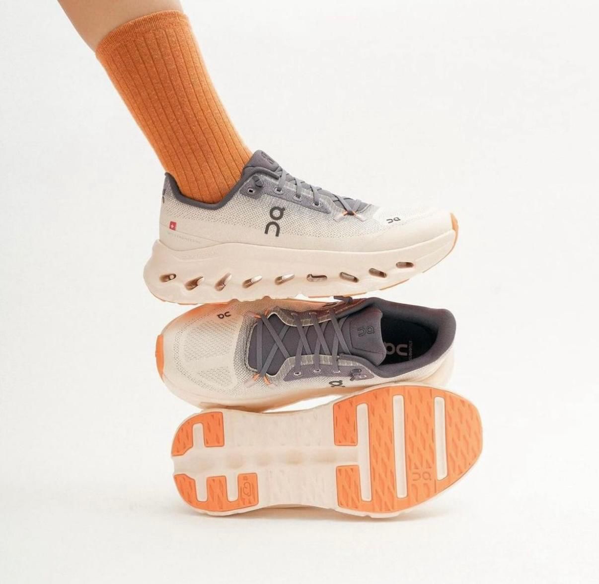WhatsApp_Image_2025-01-22_at_13.03.29 | AE JERSEY Pair of On running shoes in gray and orange, stacked mid-air with an orange sock visible above.