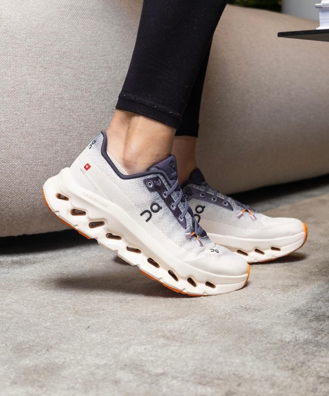 WhatsApp_Image_2025-01-22_at_13.03.38 | AE JERSEY Light gray On running shoes with thick white soles and orange tips, worn by a person in black leggings on a carpeted floor.