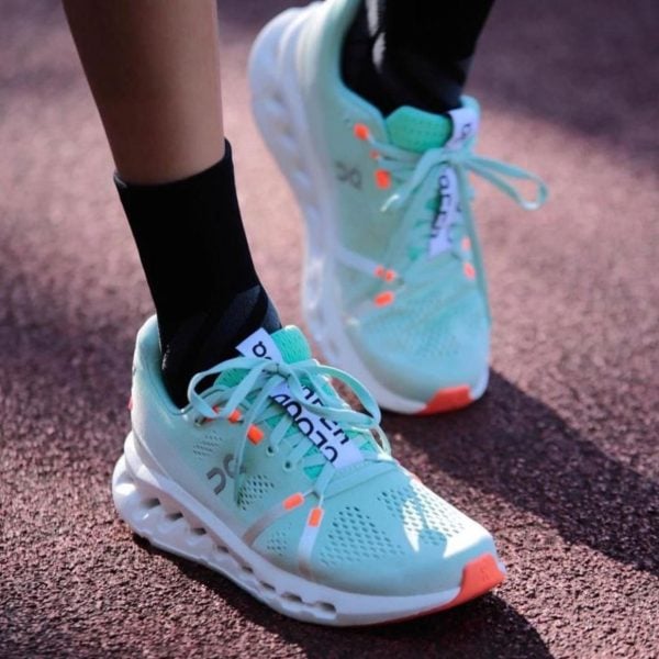 Teal running shoes with white soles on a track, laces tied, close-up of feet in black socks.