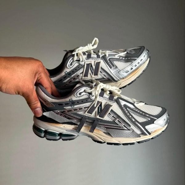 Hand holding a pair of gray and white New Balance running shoes with white laces and black accents