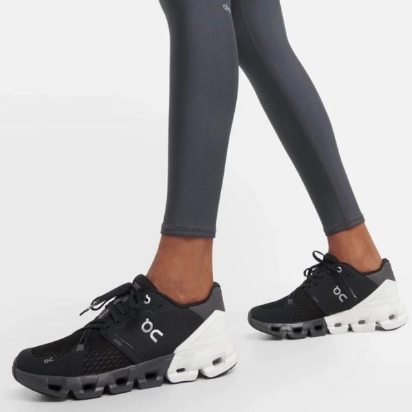 Black athletic sneakers with white chunky soles worn with dark leggings, side view showing logo 'on' and perforated upper details for a fitness look.