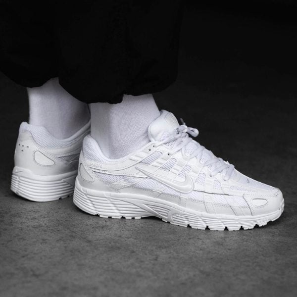 White athletic sneakers worn with white socks, standing on a gray surface in a monochrome shot.