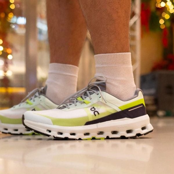 Close-up of white and lime-green running shoes with gray laces, worn with light gray socks.
