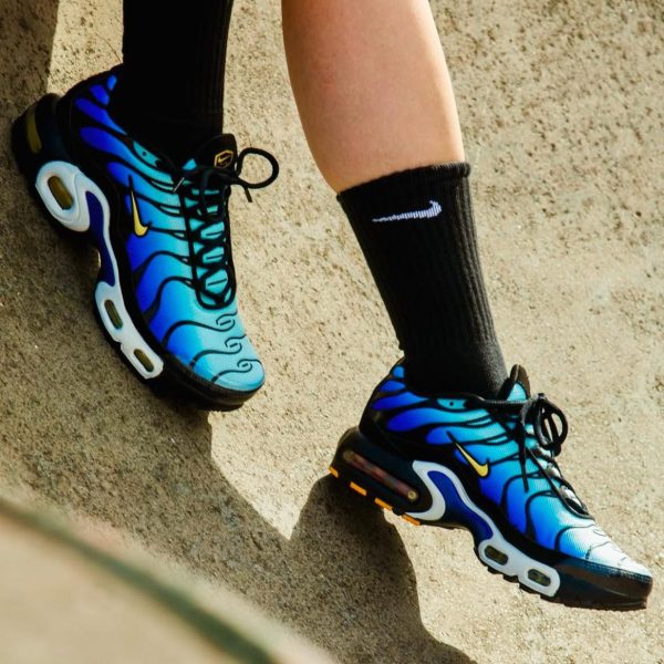 Pair of blue gradient running shoes with black laces on a sandy surface, mid-step motion showing sole details