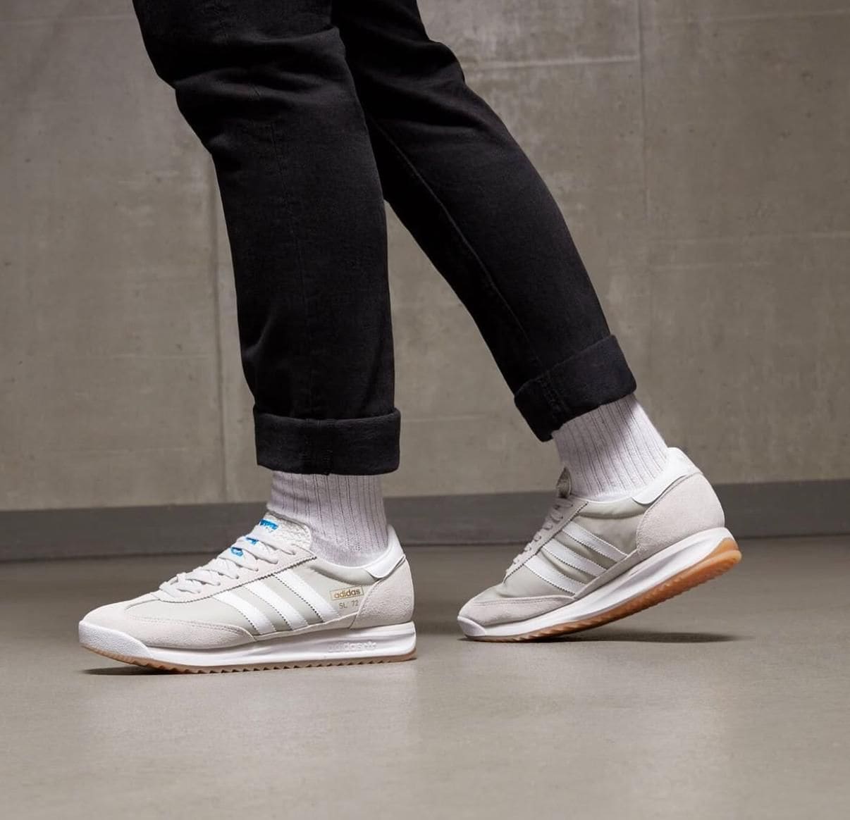 WhatsApp_Image_2025-04-08_at_14.47.32 | AE JERSEY Person wearing white Adidas sneakers with light brown gum soles, gray socks, and black rolled-up jeans standing indoors on a smooth floor.