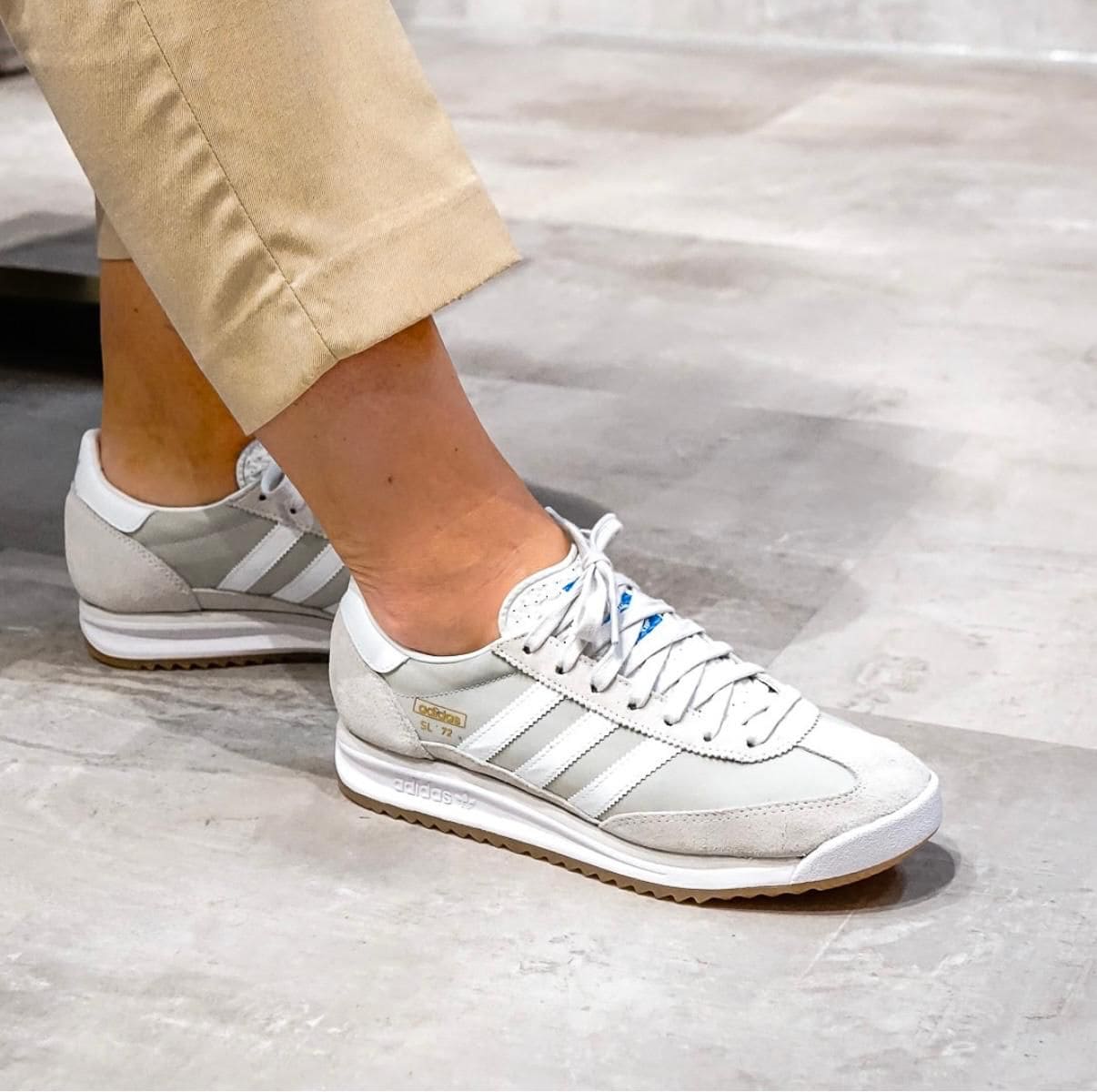 WhatsApp_Image_2025-04-08_at_14.47.52 | AE JERSEY Close-up of a person wearing light gray Adidas sneakers with white stripes and beige cuffed pants, standing on a concrete floor.