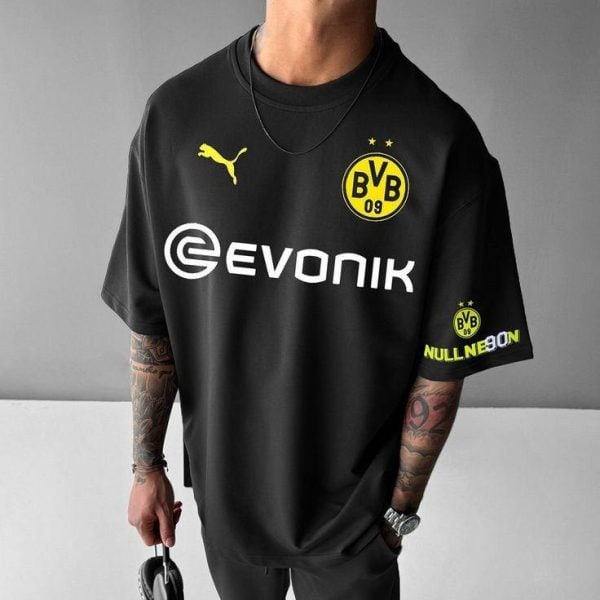 Person wearing a black Borussia Dortmund soccer jersey with Evonik sponsor and yellow club crest, standing against a gray wall.