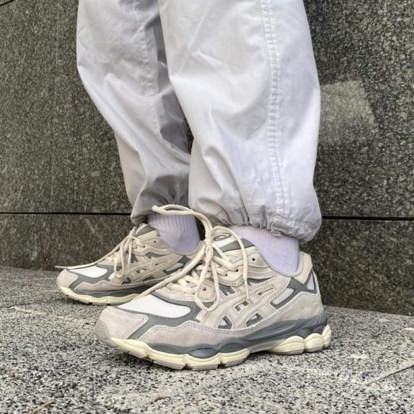 Person wearing light gray pants and white socks standing on a stone ledge, wearing beige/gray athletic sneakers with laces.