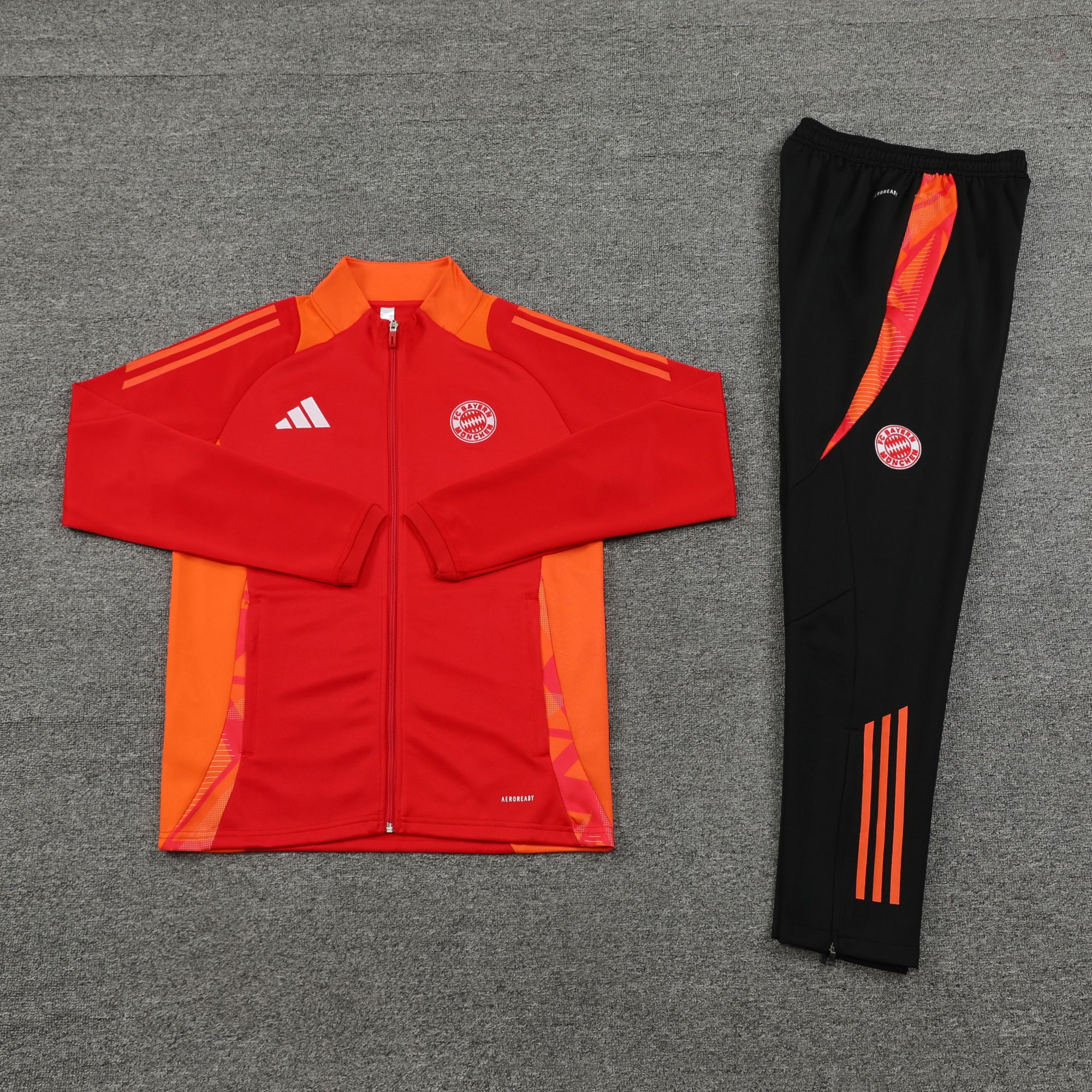 a131402f | AE JERSEY Red FC Bayern Munich jacket with zipper, paired with black track pants featuring orange side stripes on a gray carpet.