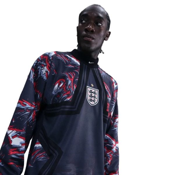 Young man wearing a dark England football jersey with a red-blue patterned outer layer, looking off to the side.