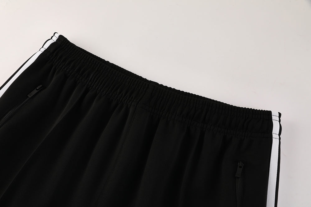 a2a7998b | AE JERSEY Close-up of black athletic track pants with an elastic waistband and white side stripes, showing zippered pockets on each side.