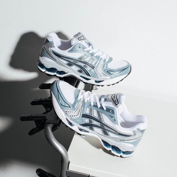 Pair of white and light blue running shoes with teal accents resting on a metal exercise stand.