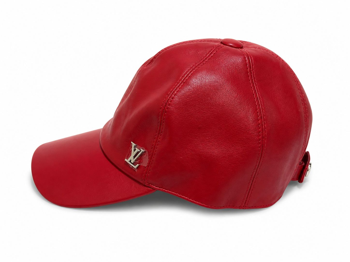 a802e301-9d87-4f35-ac7b-af9754442d65 | AE JERSEY Red leather baseball cap with a silver LV logo on the front panel placed against a white background, side view.