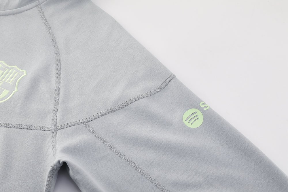 a9233c68 | AE JERSEY Close-up of a light gray sweatshirt sleeve with visible seam lines and a lime-green circular logo on the upper arm, plus a partial shield emblem on the chest area.