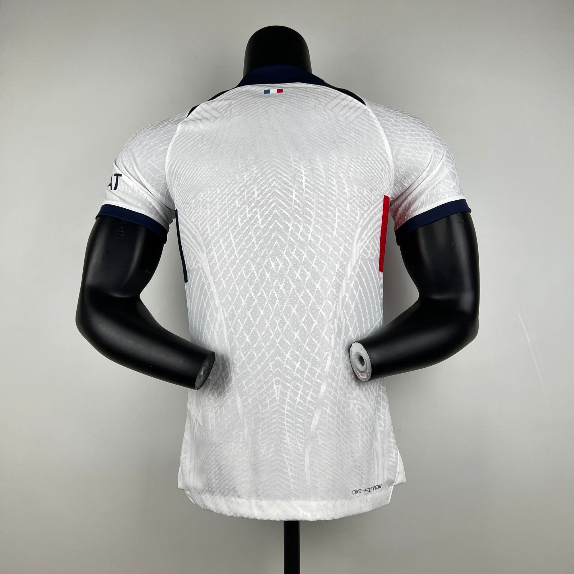 ad3ad583_504f44af-2507-4a68-a09a-acbbbfde848f | AE JERSEY Back view of a white patterned sports jersey on a black mannequin torso, small French flag at the neckline.