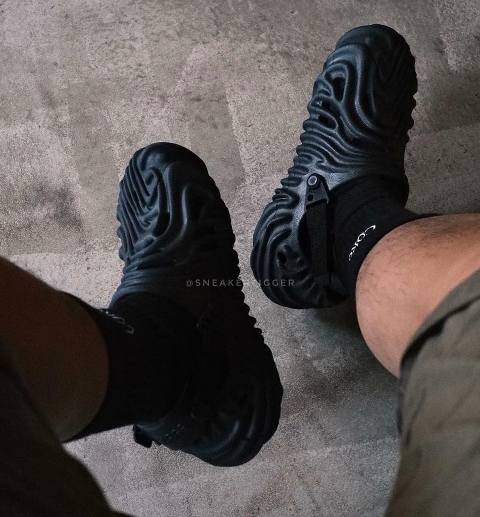 ad95717a-3570-47f7-b152-a143f1b6332d | AE JERSEY Top-down view of two black chunky-soled sneakers worn with black socks on a concrete floor