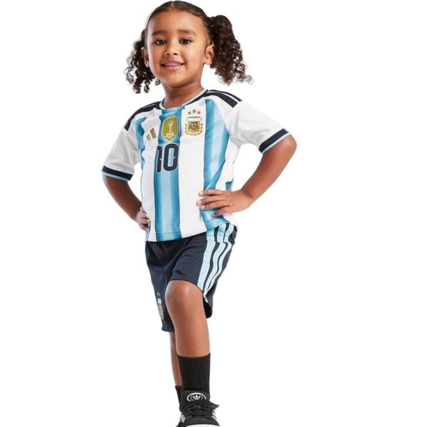 Smiling young girl in an Argentina soccer jersey (blue and white stripes) with number 10, standing with hands on hips in navy shorts and socks.