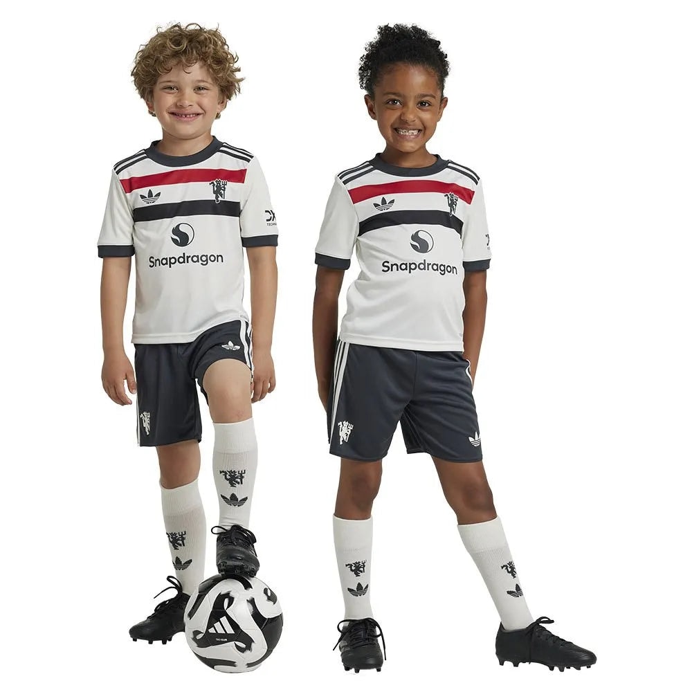 adidas-manchester-united-24-25-junior-third-set | AE JERSEY Two smiling children in matching white soccer uniforms stand together with a soccer ball at their feet, ready to play.