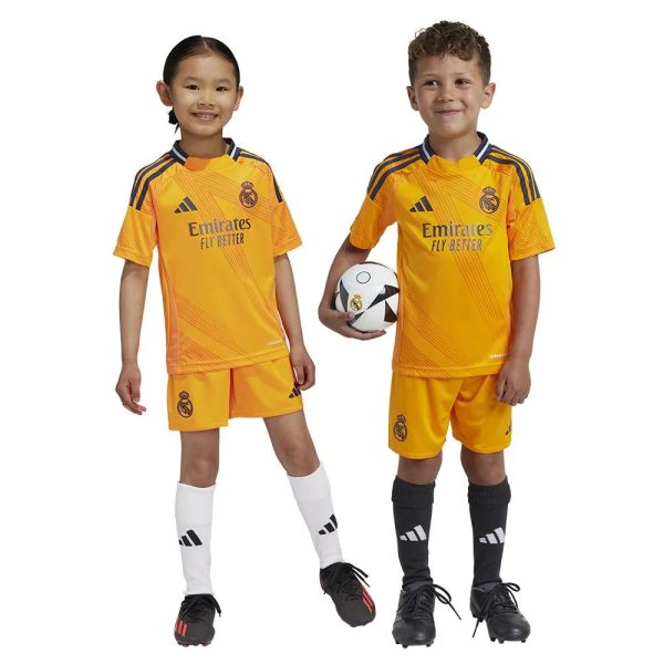 Two young children wearing yellow Real Madrid soccer jerseys stand side by side, one holds a soccer ball.
