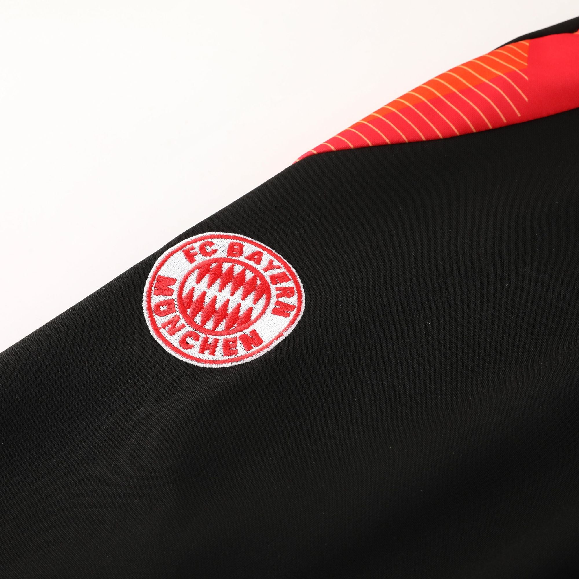 ae8efb96 | AE JERSEY Close-up of a red-and-white Bayern Munich crest embroidered on black fabric, partially visible along a diagonal seam.