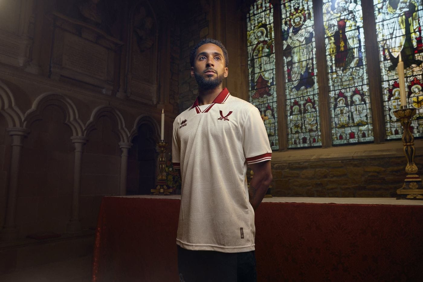 ao4yMLuh3NAtIEr | AE JERSEY Man in a white polo with red trim stands inside a church, near a red altar, with stained-glass windows behind him.