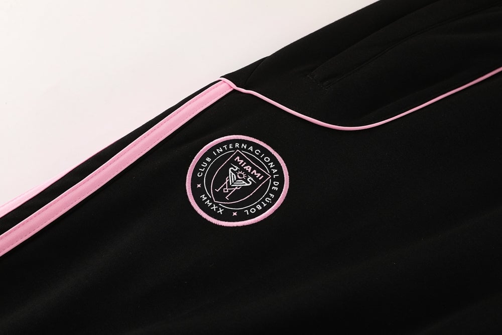 b05a39a6 | AE JERSEY Close-up of black athletic jacket with pink piping and an embroidered circular logo behind the seam.