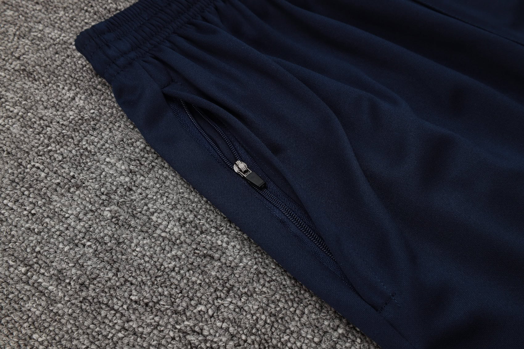 b16ef854 | AE JERSEY Close-up of navy blue fabric with a zipper along a seam, lying on a gray carpet.