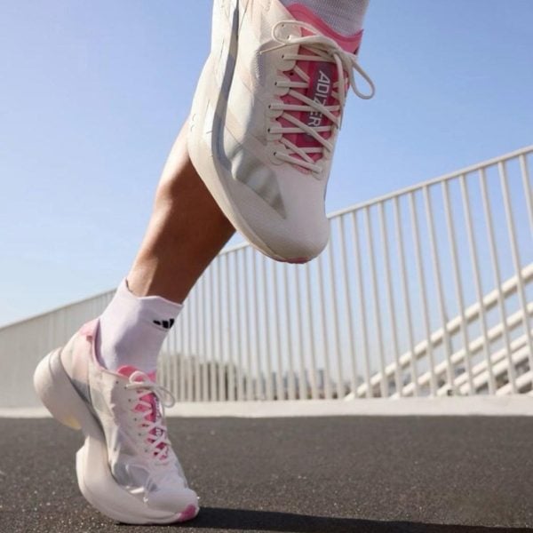 Close-up of white and pink athletic shoes in mid-step on a paved path with a railing in the background