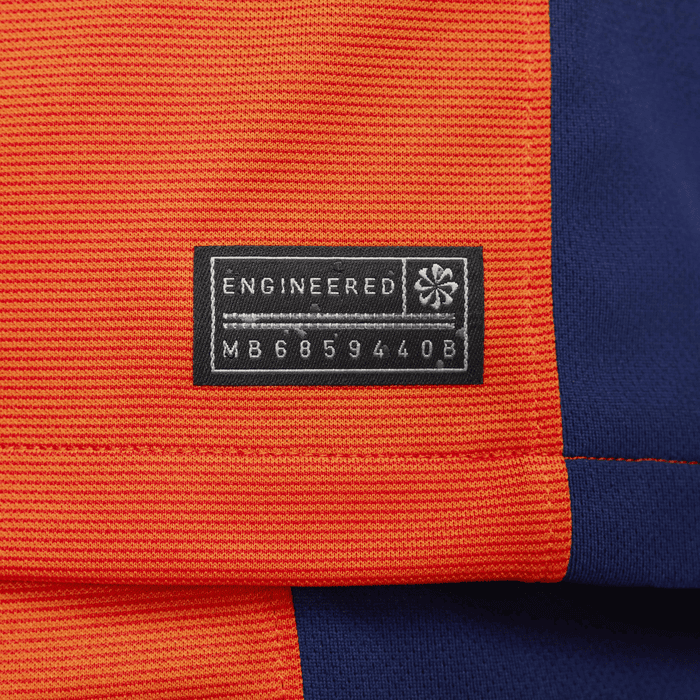 b5c2c792_a8d0_4a64_9b4e_733ec69a078c_1 | AE JERSEY Close-up of orange fabric with a black label: ENGINEERED and a serial code MB68594408 beside blue fabric.