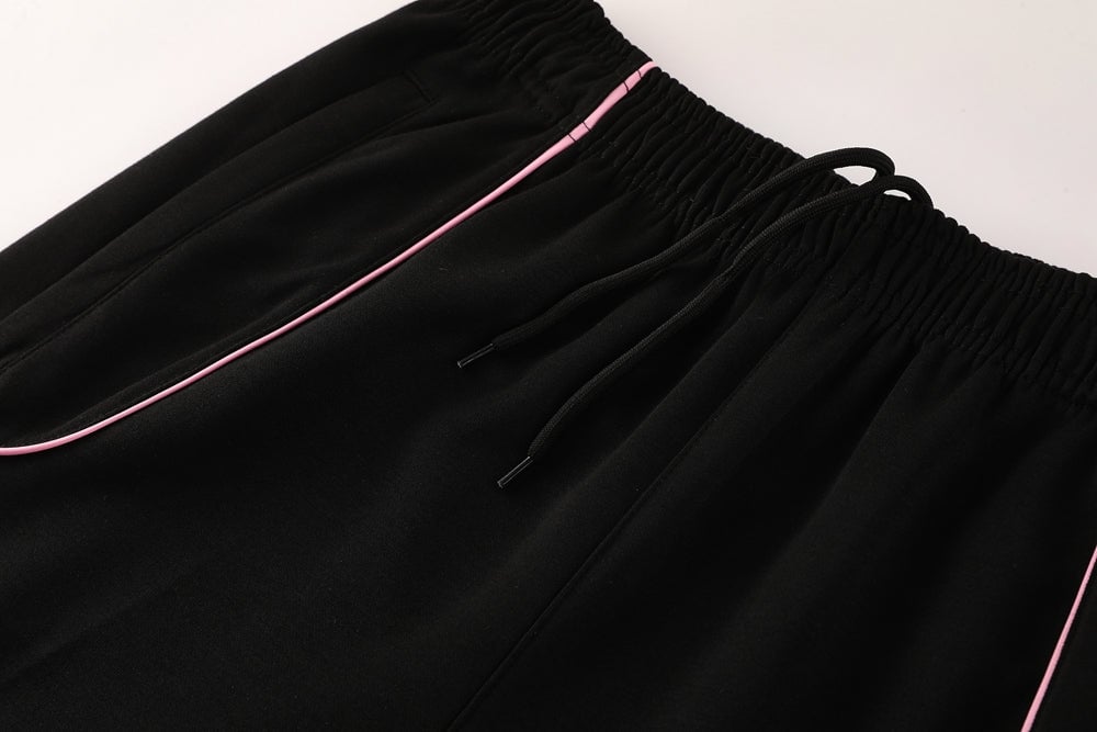 b64b0118 | AE JERSEY Close-up of black jogger pants with pink piping along the pocket seam and a drawstring elastic waist.