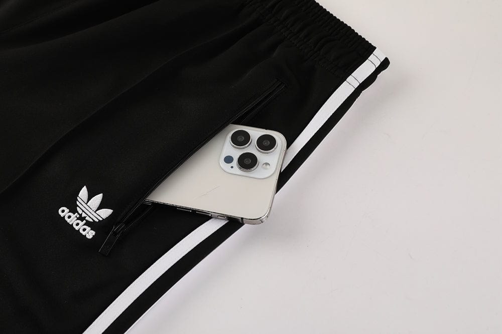 b64fd50c | AE JERSEY Black Adidas track pants with white side stripes and a zip pocket holding a smartphone.