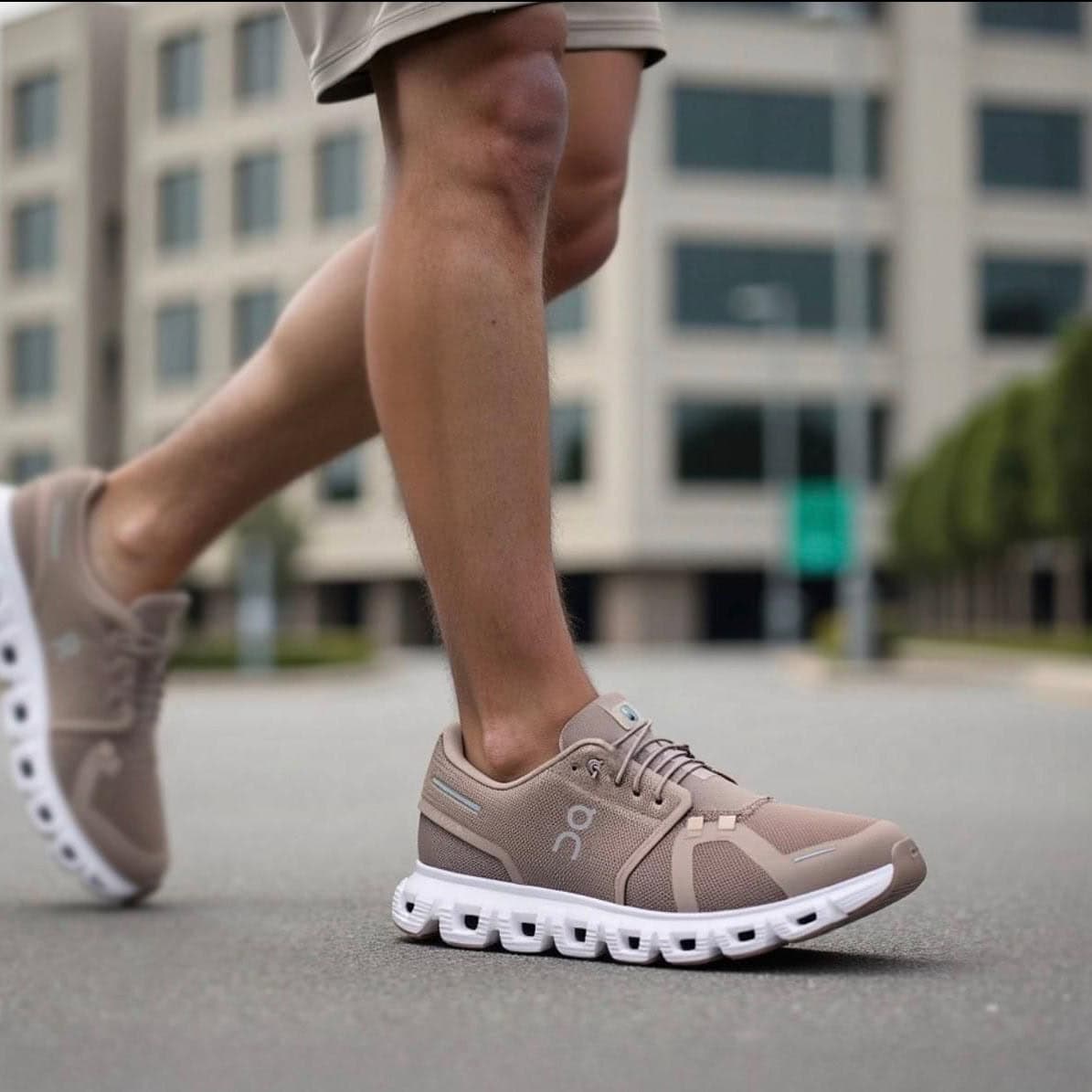 b837e654-ed9c-4689-ac68-8123bc121ec1 | AE JERSEY Close-up of a person wearing beige athletic running shoes stepping on pavement with an urban background behind them, mid-stride.