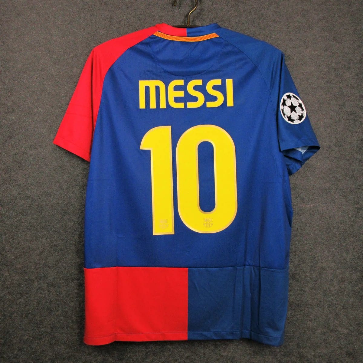 barcelona-classic-2009-final-with-messi-10-jersey-783840 | AE JERSEY Blue Barcelona football jersey hanging on a hanger, 'MESSI' and large yellow number 10 on the back with a Champions League patch on the sleeve. The jersey has red and blue color blocks.