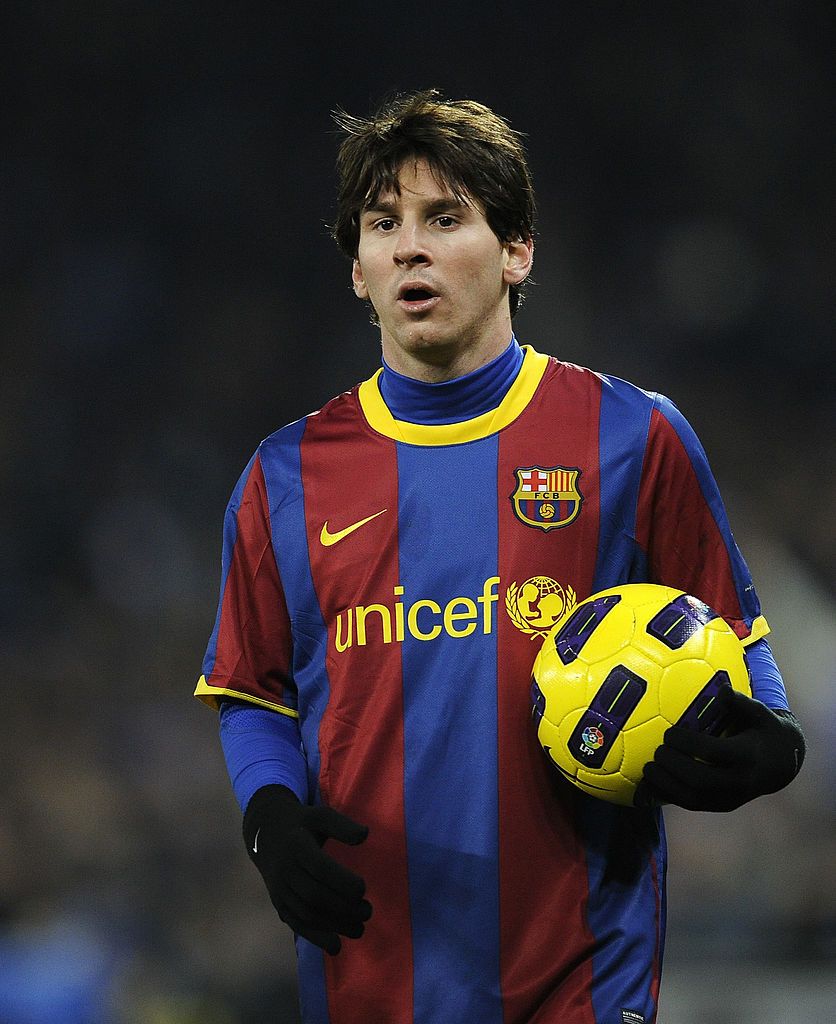 barcelona-classic-201011-final-with-messi-10-badges-jersey-659979 | AE JERSEY Soccer player in a Barcelona jersey holding a yellow soccer ball on the field.”