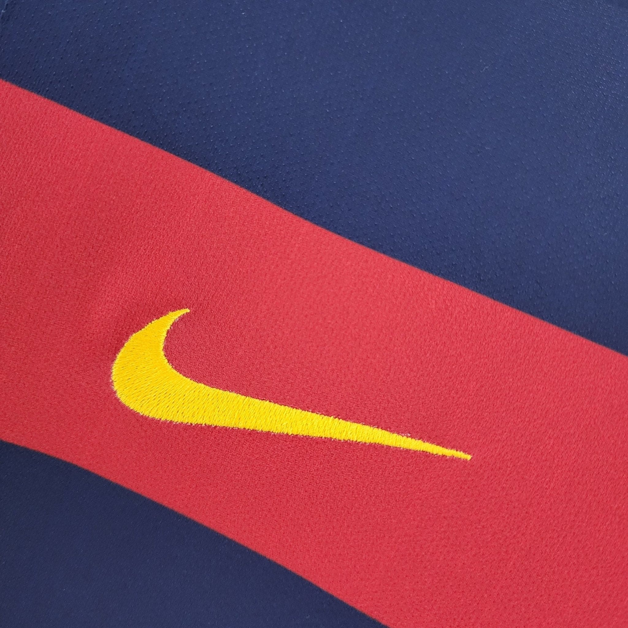 barcelona-classic-201516-final-with-messi-10-badges-jersey-491035 | AE JERSEY Close-up of blue and red fabric in a diagonal layout with a partial yellow curved line visible at the edge.